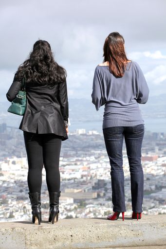 A back shot of two women standing in the high place and looking to the city