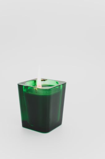 isolated burning scented green candle in a glass on a white background