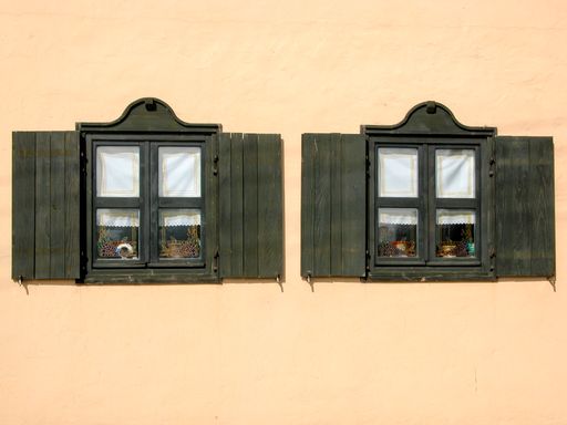 A closeup of two old black wooden windows with open shutters on a mate light background