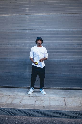 A shot of an African man with white t shirt and a black hat posing for the camera in the street, Spain