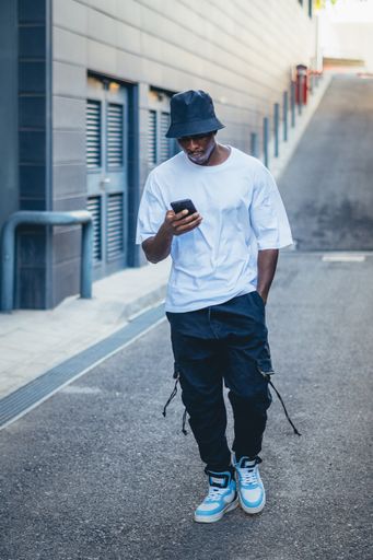 A vertical shot of a model casual young Black male with a blue hat checking his phone outdoors