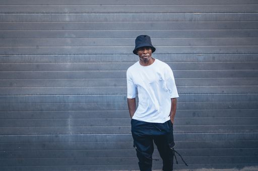 A shot of an African man with white t shirt and a black hat posing for the camera in the street, Spain
