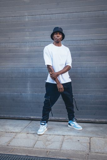 A vertical shot of a model casual young Black male with a blue hat posing in the street outdoors