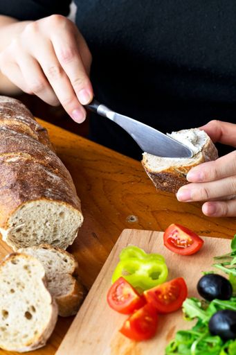 A vertical shot of organic bread on a wooden table and a hand smearing butter with a kitchen knife