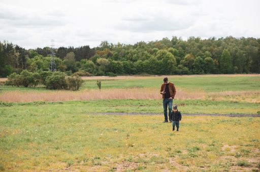 A beautiful view of a man and a small child standing on a green grass field close by a forest