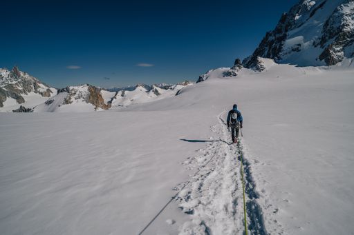 An Alpinist walking on a glacier. Mountaineering in Mont Blanc Masiff, high mountain alpine landscape with snow, ice and high peaks. Climber with rope