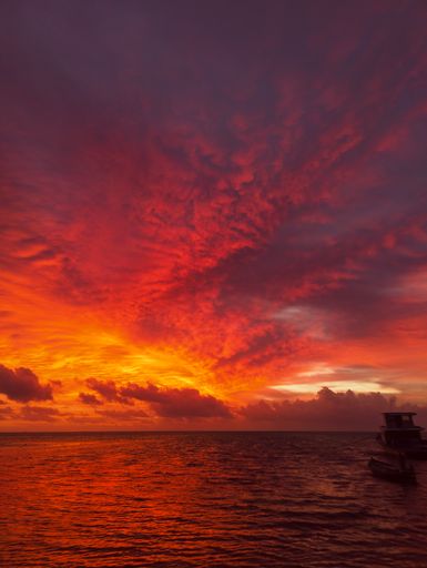 A mesmerizing scene of silhouetted boat in the water against an orange cloudy sky at sunset