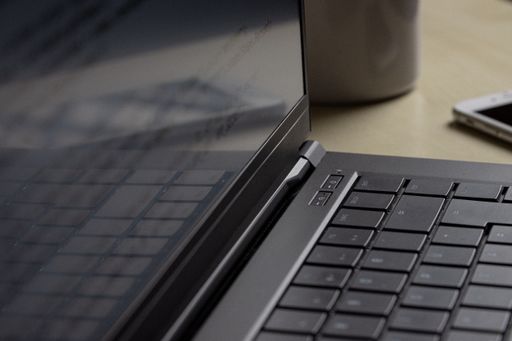 A close up of a keyboard of a black laptop with a reflecting screen on a wooden table