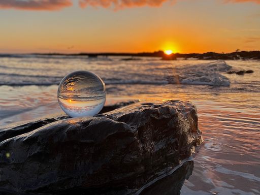 A glass ball on a rock reflecting the ocean at sunset