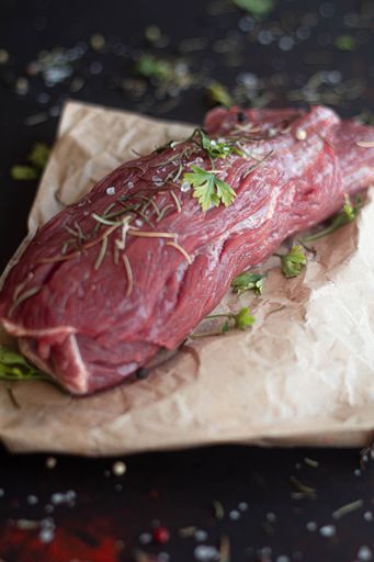 A vertical shot of beef on a board in a kitchen