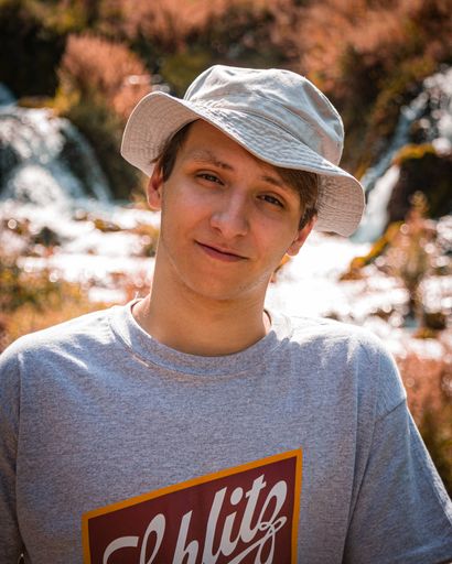 A vertical shot of a young male in a hat smiling near a river in Spearfish, USA
