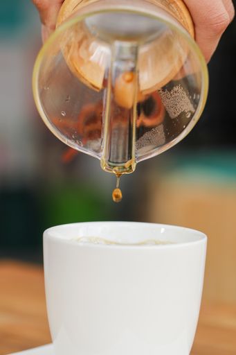 A vertical shot of the last coffee drop pouring from a manual pour-over coffeemaker into a cup