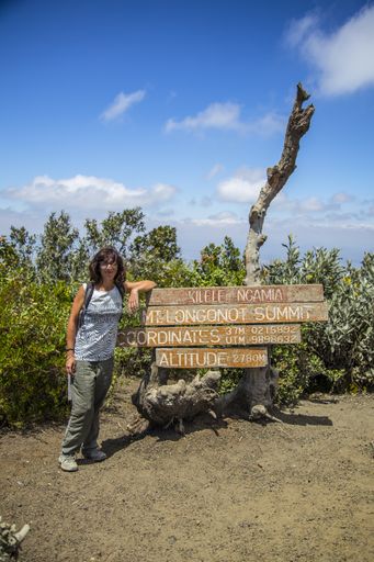 A vertical shot of a female standing by a sign of Longonot National Park captured in Longonot, Kenya