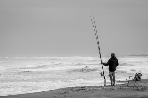 A grayscale shot of a fisherman fishing in Emerald Isle surrounded by the Ocean in North Carolina