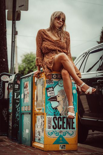 A stylish female in sunglasses sitting on a newspaper box in Nashville, USA