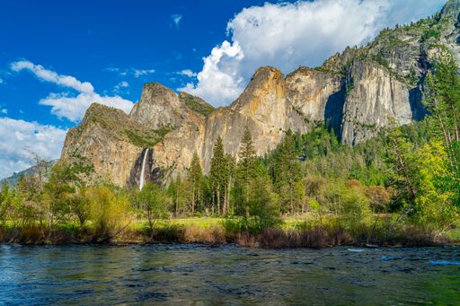 A scenic view of Yosemite National Park with lush greenery, majestic cliffs, and a river under a vibrant blue sky.
