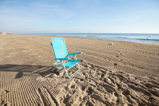 A solitary blue beach chair on a sandy beach with a calm sea and clear sky, conveying tranquility and solitude.