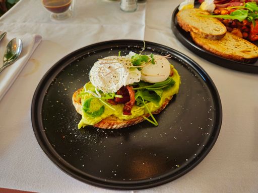Delicious avocado toast with poached eggs and greens on a black plate, perfect for a healthy brunch.
