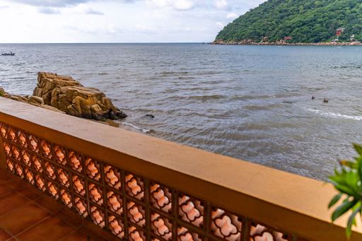 Coastal view from a balcony with decorative railing overlooking the sea and rocky shoreline under a partly cloudy sky.