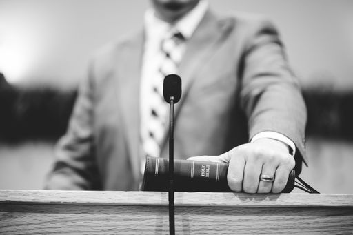 A grayscale closeup shot of a male speaking  from podium Holy Bible  hold in hand