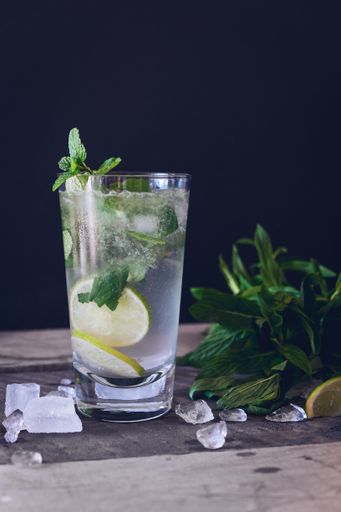 A vertical selective closeup shot of ice lemonade with lime in a glass cup on a black background
