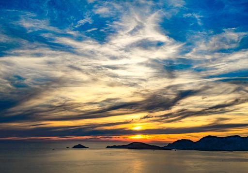 Dramatic sunset over a serene sea with vibrant clouds and distant islands on the horizon.