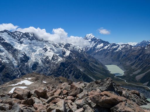 Panoramic view of snow-capped mountains and a valley with a glacial lake under a clear blue sky in New Zealand.