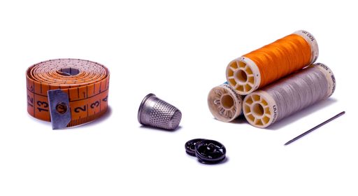 Thimble, thread spools, needle, and measuring tape on white perfect for sewing, textile, and DIY themes.