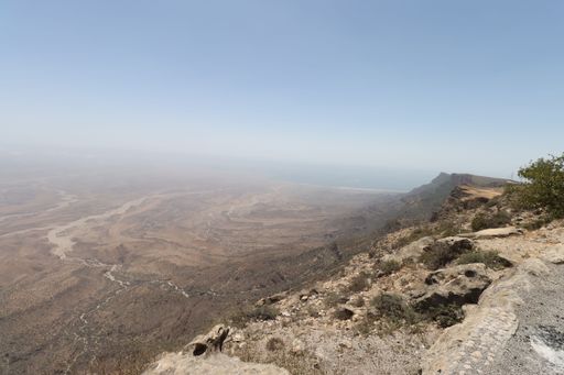 Expansive view of a rocky desert landscape with a clear sky and distant mountains in the background.