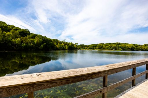 A wooden bridge over the reflective clean lake Carver surrounded by dense trees in Minnesota