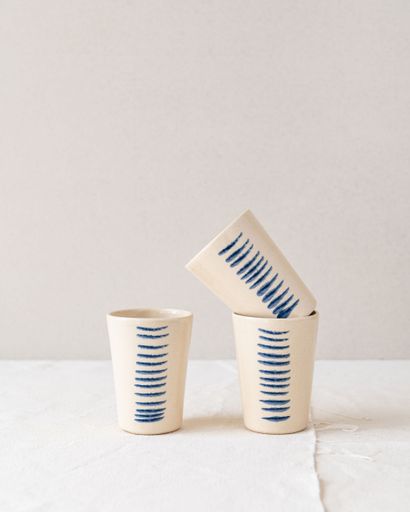 Three ceramic cups with blue line patterns arranged on a white fabric background, showcasing minimalist design.