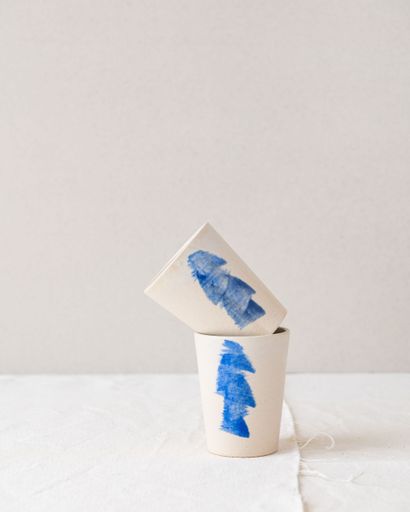 Minimalist design of two ceramic cups with blue abstract paint on a neutral background.