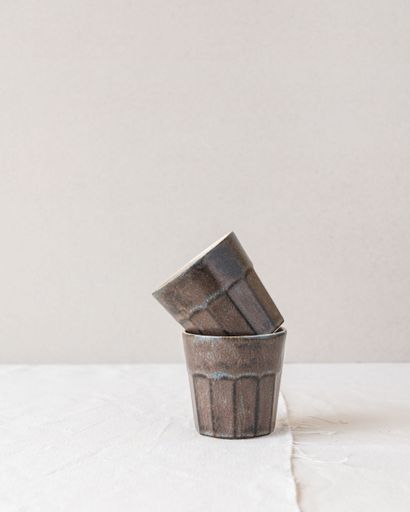Two rustic ceramic cups stacked on a textured white surface against a neutral background.