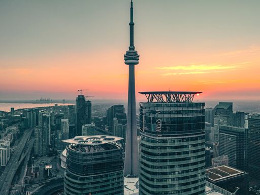 Aerial view of Toronto's skyline with the CN Tower at sunset, showcasing modern skyscrapers and a vibrant sky.
