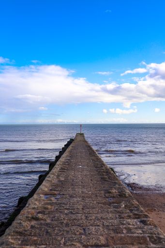 A vertical shot of a long pier in the sea under the cloudy sky