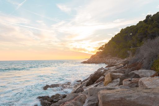 A gorgeous view of a bright sun shining through clouds obscuring it in an orange sky at the beach