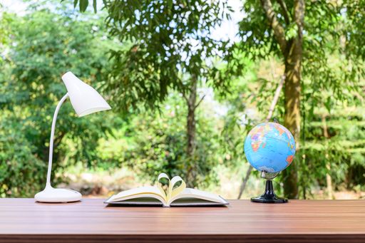 A heart-shaped page of a book, lampshade, and globe on a wooden table outdoors