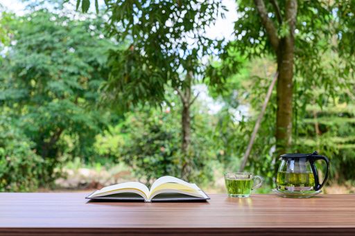 An open book,and green tea on a wooden table outdoors