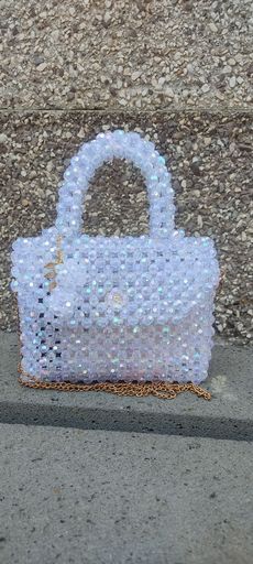 A stylish beaded handbag with a shimmering design, featuring a clear and gold chain, set against a textured stone background.