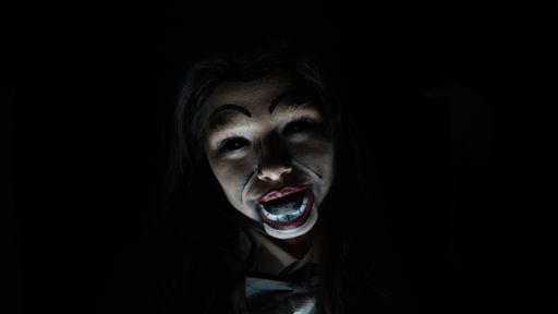 A scary possessed girl with a creepy doll makeup in a dark room - horror concept