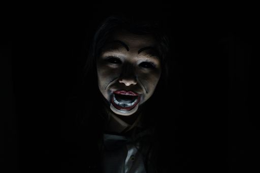 A scary possessed girl with a creepy doll makeup in a dark room - horror concept