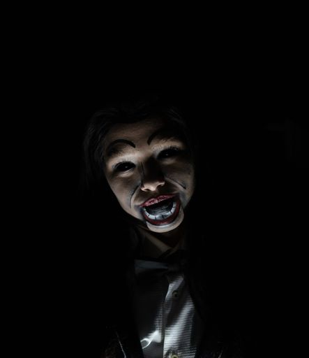 A scary possessed girl with a creepy doll makeup in a dark room - horror concept