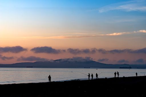 The silhouettes of people fishing near the shore of the Black Sea in Bulgaria with smoky clouds during sunset