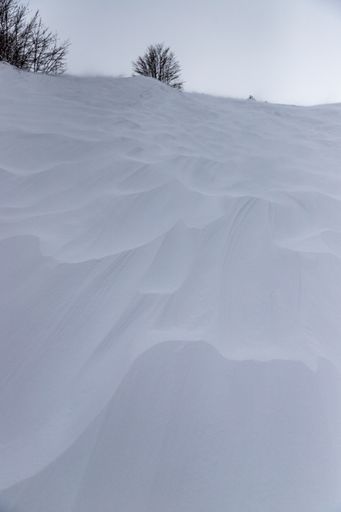 A vertical shot of pistes on hills covered in the snow under a cloudy sky