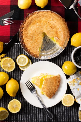 A vertical top view of a lemon and blueberry pie with a slice surrounded by lemons on a wooden table