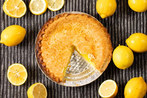 A top view of a lemon pie with a slice cut out surrounded by lemons on a wooden table