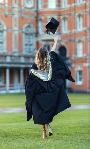 A vertical shot of a girl throwing her graduation hat in the air