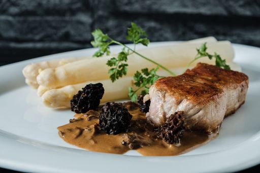 A tasty veal steak with asparagus and morels on a plate
