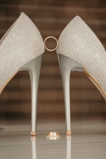 A closeup of engagement rings between the high heels of a bride