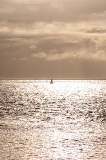 A vertical shot of a single boat sailing on the sea during a sunset